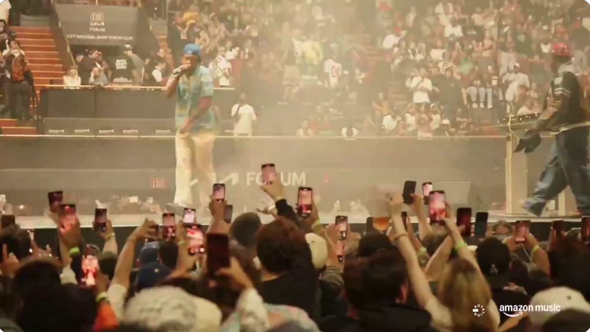 Crowd at a concert filming the performance on their phones while artists perform on stage