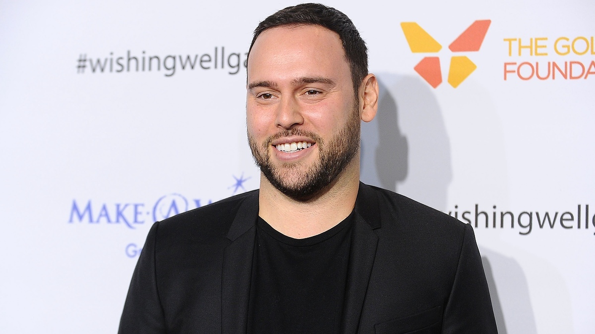 Smiling man in a suit at an event with logos in the background. #wishingwell is seen behind him