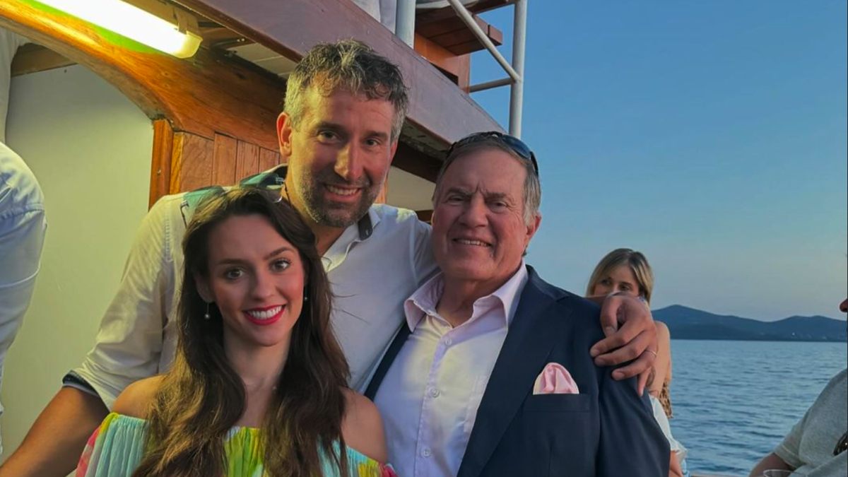 I don't know any of the individuals in the image. A man stands in the center, having his arm around another man hanging on this man's shoulders. A woman in a dress stands to their right. They are on a boat with multiple people in the background