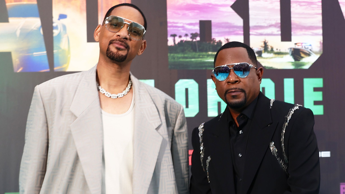 Will Smith and Martin Lawrence at the red carpet premiere, both wearing sunglasses and stylish suits, standing in front of a movie poster backdrop