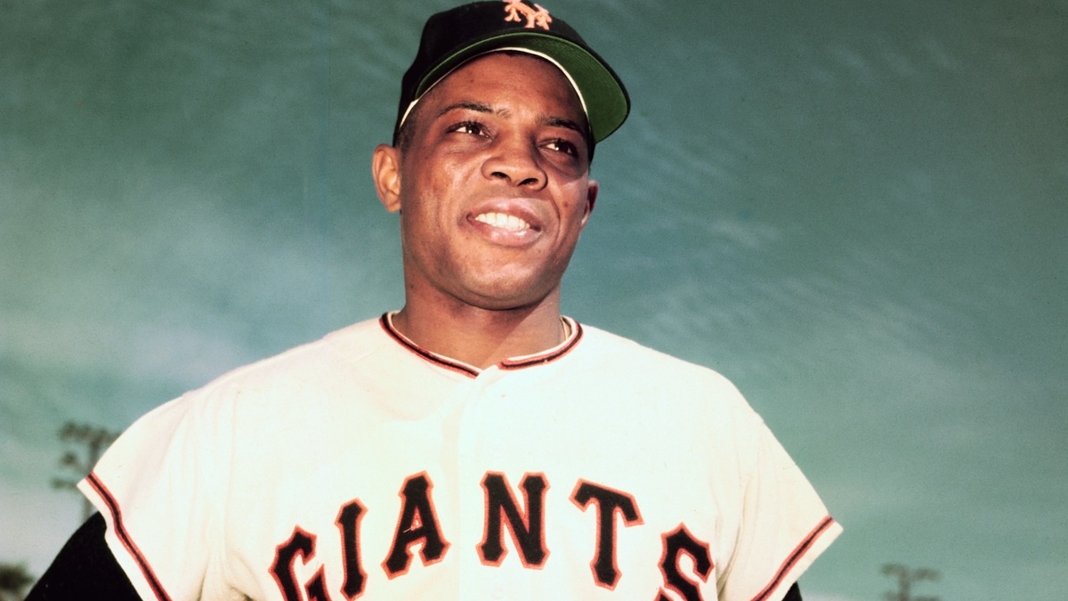 A person is wearing a Giants baseball uniform and a cap with an "NY" logo, showing a confident expression against a clear sky backdrop