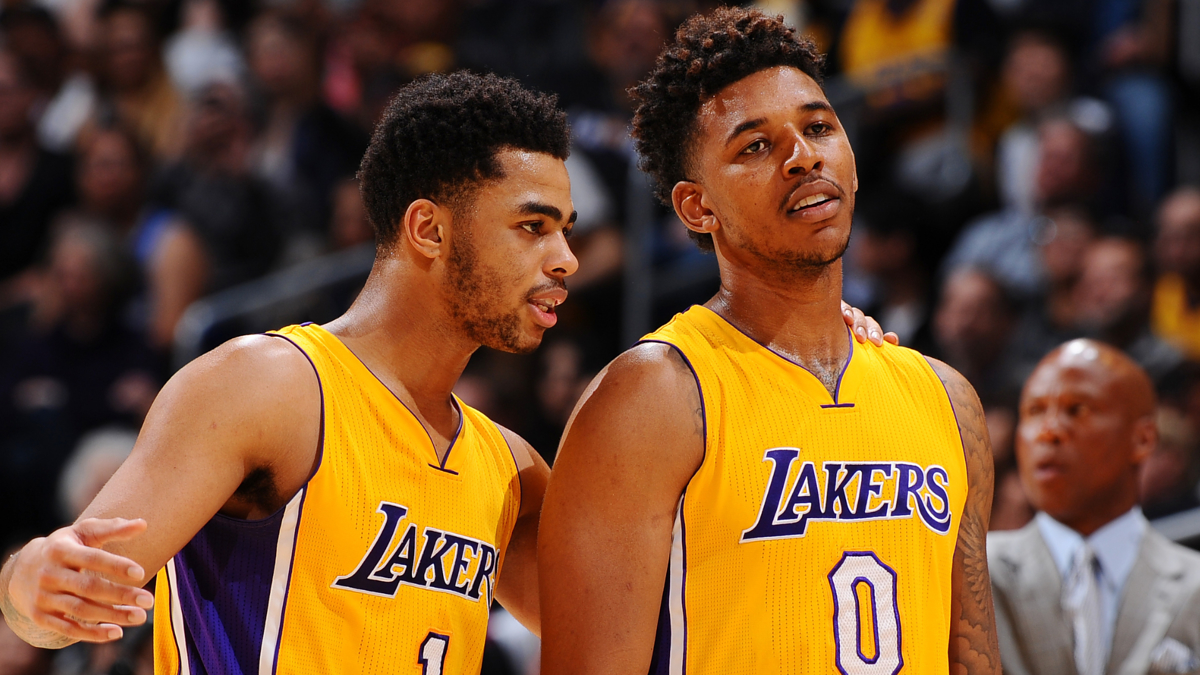 Two basketball players in Lakers jerseys talking on the court with spectators in the background