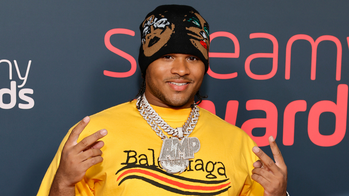 A man in a yellow Balenciaga shirt and patterned beanie poses at the Streamy Awards, wearing a large chain necklace.