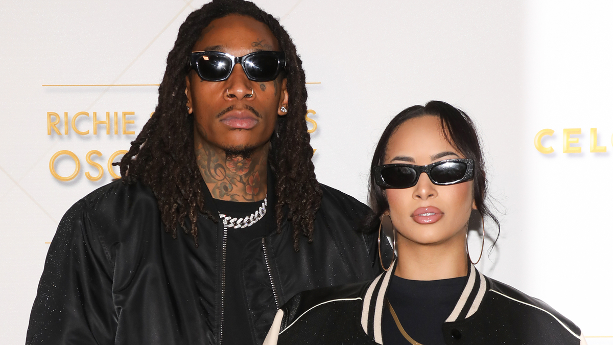 Wiz Khalifa and Aimee Aguilar pose wearing black jackets and sunglasses at an event
