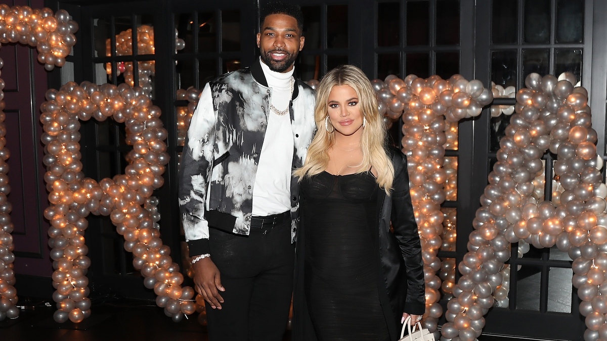 Tristan Thompson and Khloe Kardashian in formal wear, posing with a balloon arch backdrop