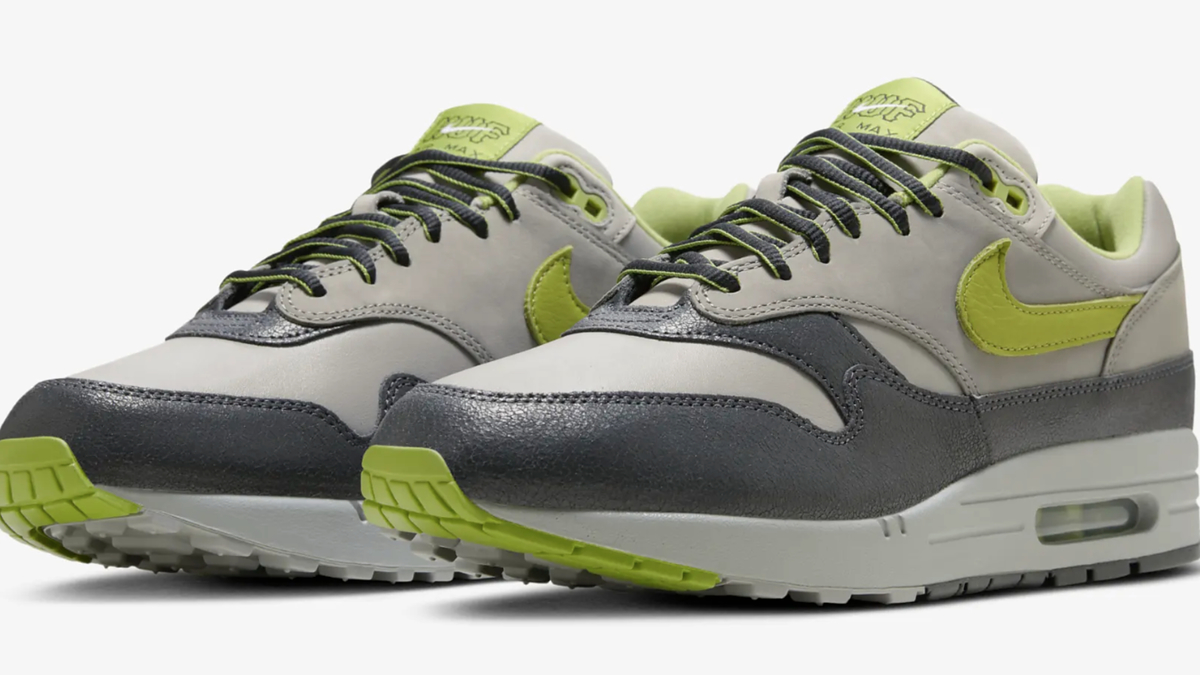 A pair of Nike Air Max 1 sneakers with a white and gray body, featuring lime green accents and a large Nike swoosh on the side