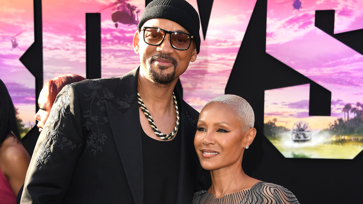 Will Smith in a black suit and Jada Pinkett Smith in a sheer, patterned dress, posing together at a "Bad Boys" movie premiere