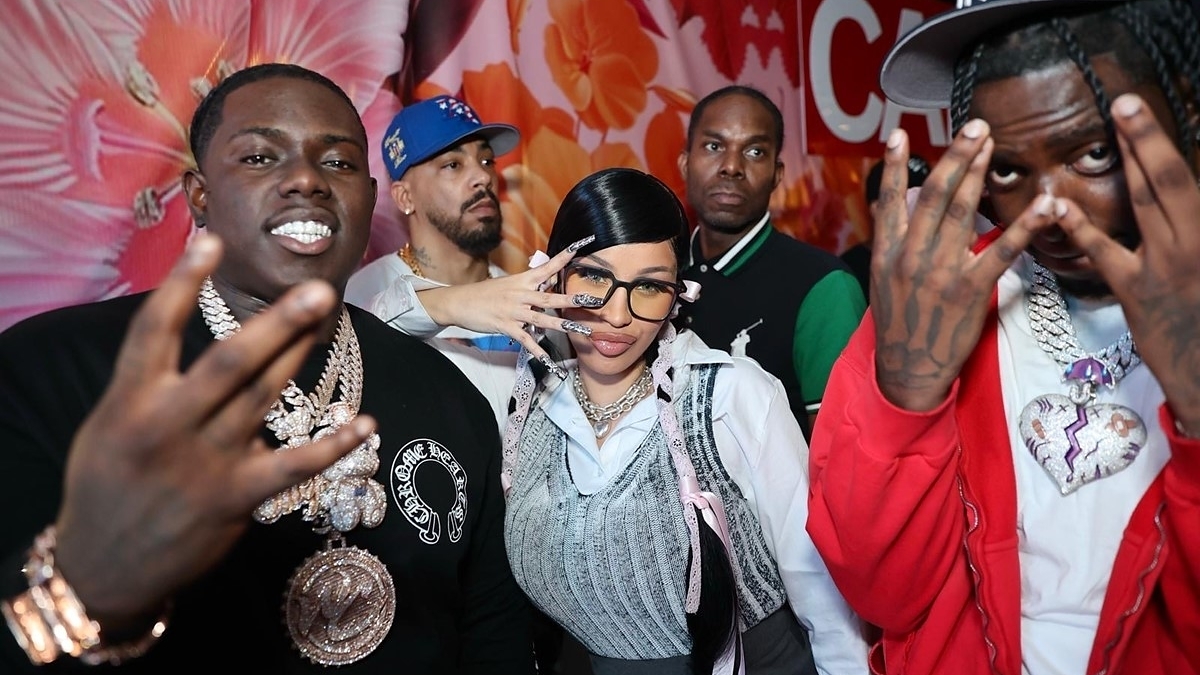 Unknown group of individuals posing with hand gestures, some wearing chains and caps, colorful floral backdrop