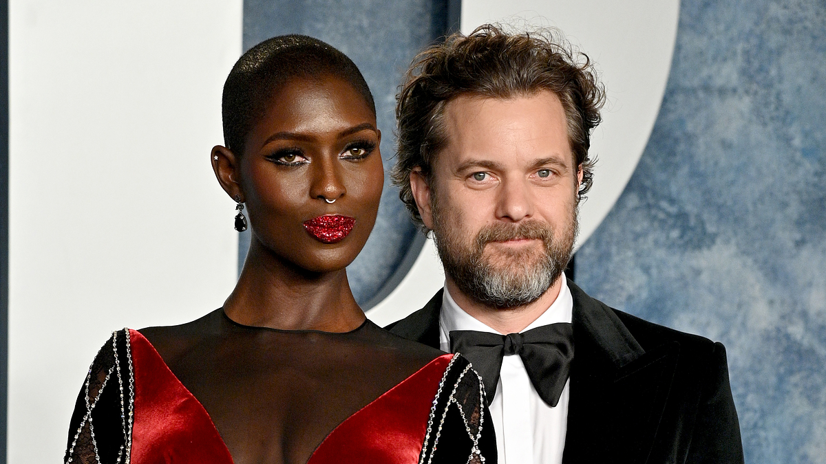 Jodie Turner-Smith and Joshua Jackson pose together on the red carpet; Jodie wears an intricate black and red gown with diamond patterns, Joshua wears a classic black tuxedo