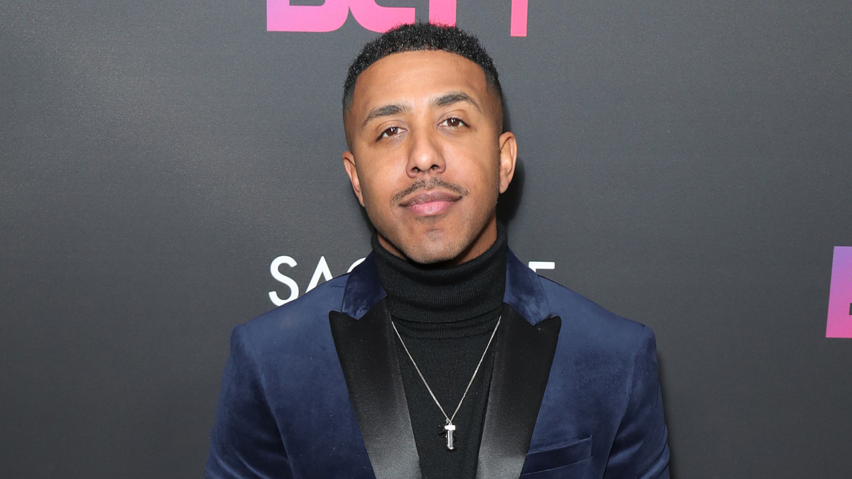 A person in a velvet blazer over a black turtleneck poses in front of a backdrop with the BET logo