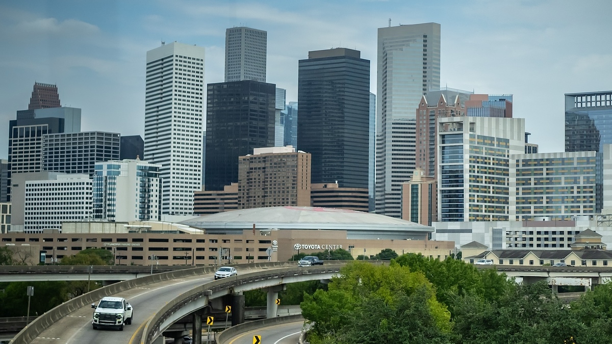 Photo of the Houston skyline with the Toyota Center in the foreground, several high-rise buildings, and multiple highways and cars