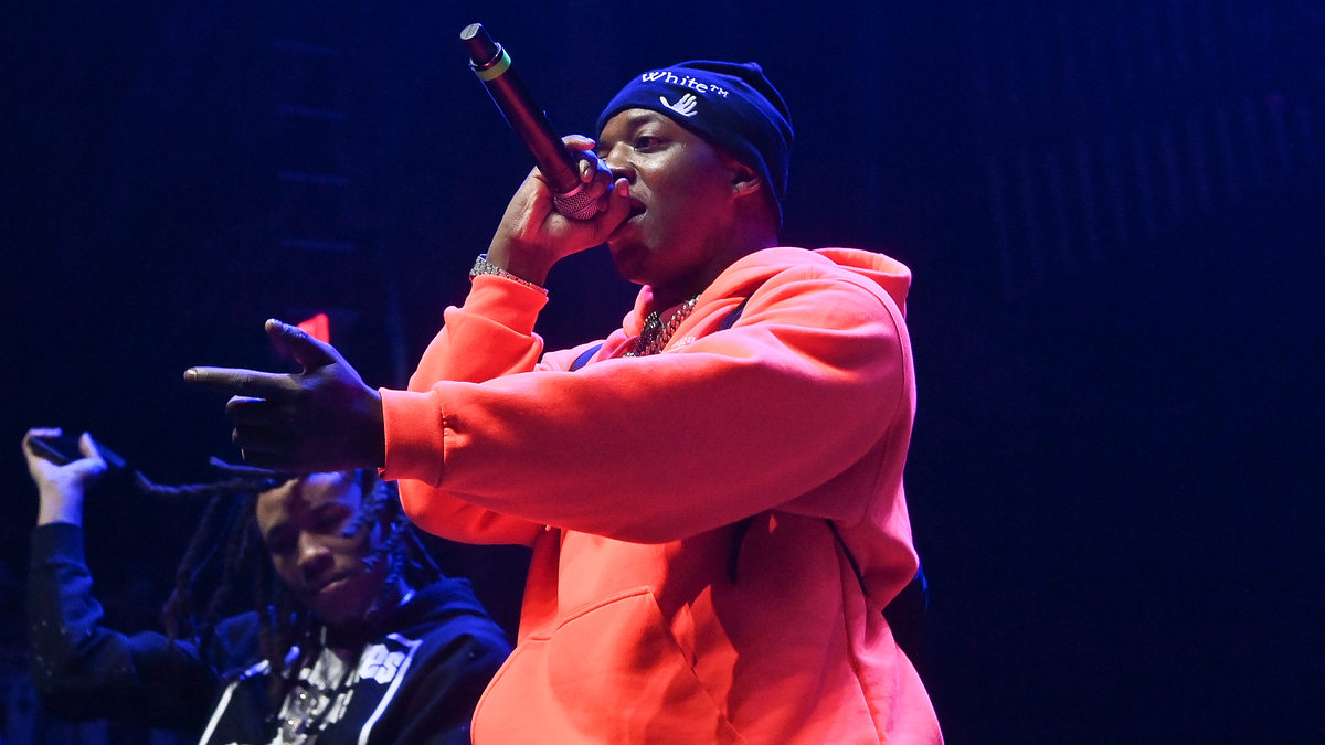 Artist performs on stage in a hoodie and beanie, holding a microphone