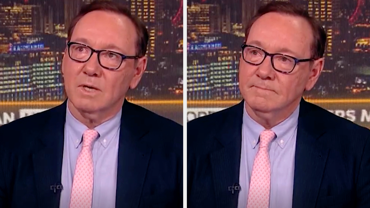 Kevin Spacey appears twice on a news program, wearing a suit, dress shirt, and tie, discussing a topic with a cityscape backdrop