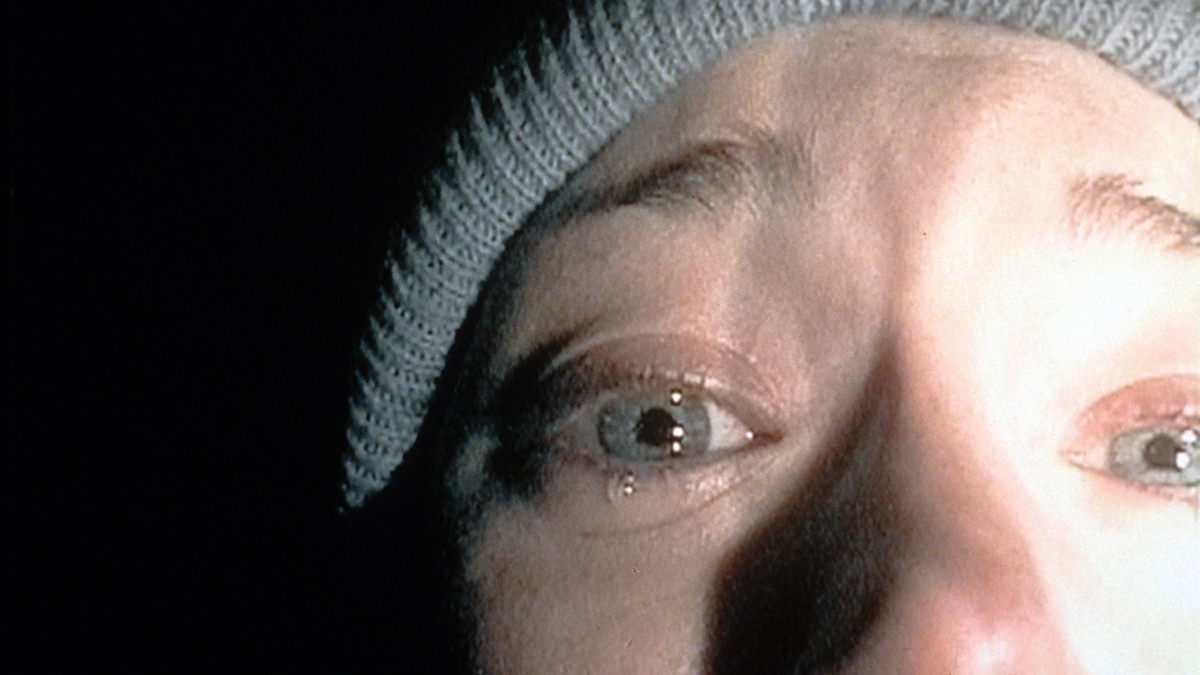 Close-up of a tearful, fearful person's face, wearing a knit beanie, in low light