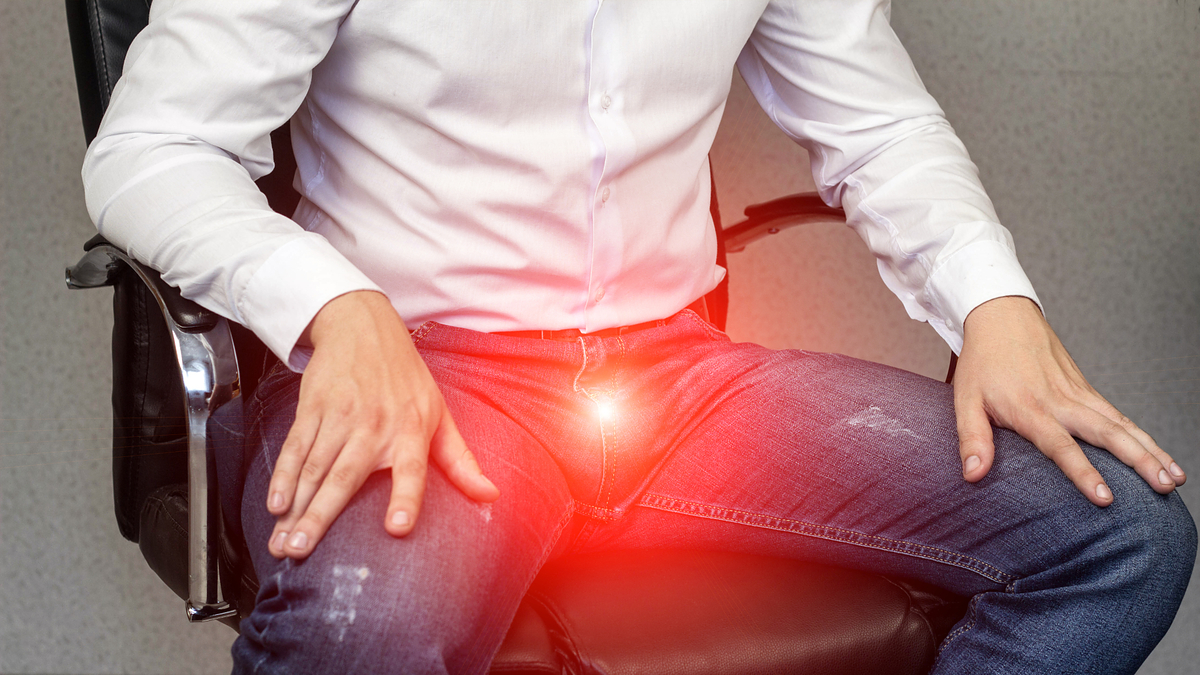 Person sitting on a chair experiencing discomfort or pain in their groin area, indicated by a glowing effect. The person's identity is not known
