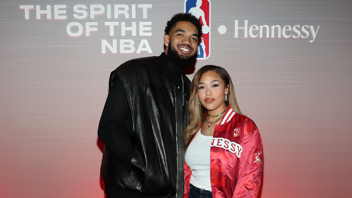 Karl-Anthony Towns and Jordyn Woods at an NBA event. Karl-Anthony wears a black leather jacket; Jordyn sports a Hennessy bomber jacket