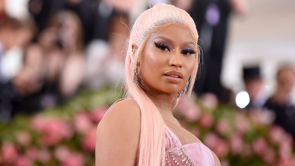 Nicki Minaj at a public event, wearing a beaded, elegant gown with her pink hair styled straight and long. She poses confidently for the camera