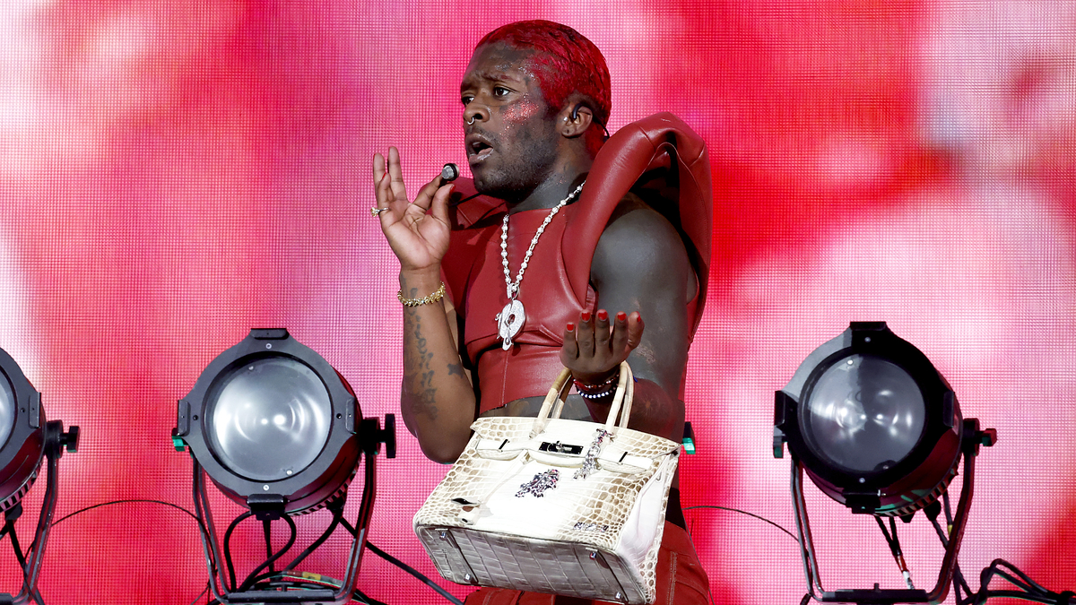 Man on stage performing, wears red outfit and holds microphone, backdrop with intense lighting