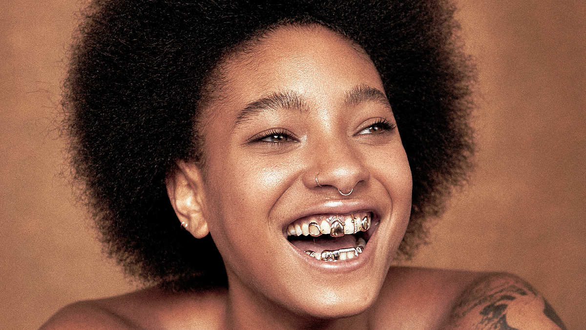 Smiling person with afro hairstyle and a visible grill on their teeth, posing for the camera