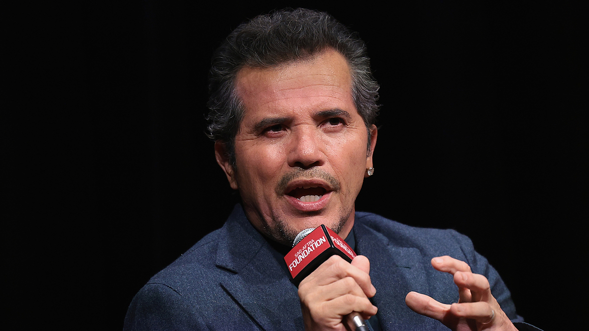 A man speaking into a microphone, wearing a suit, gesturing with his hand