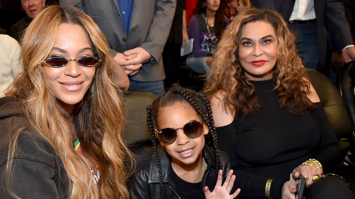 Beyoncé, Blue Ivy Carter, and Tina Knowles sit together at an event, all wearing stylish outfits and sunglasses
