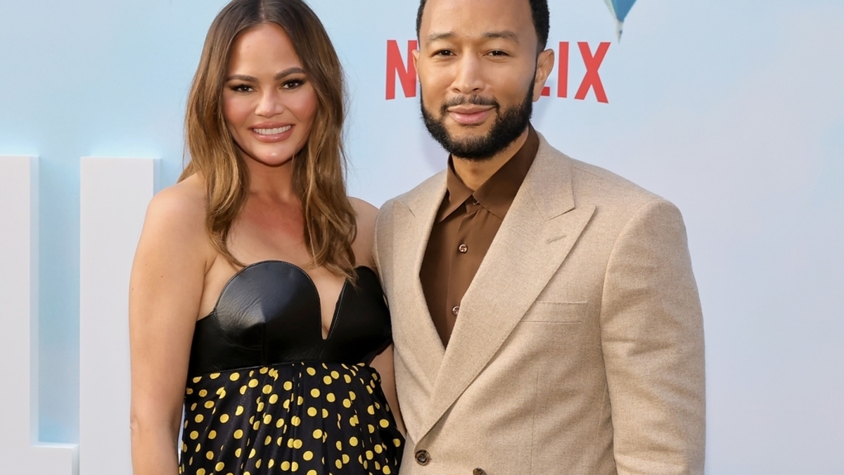 Chrissy Teigen and John Legend pose together, Chrissy in a polka-dot dress and John in a beige suit