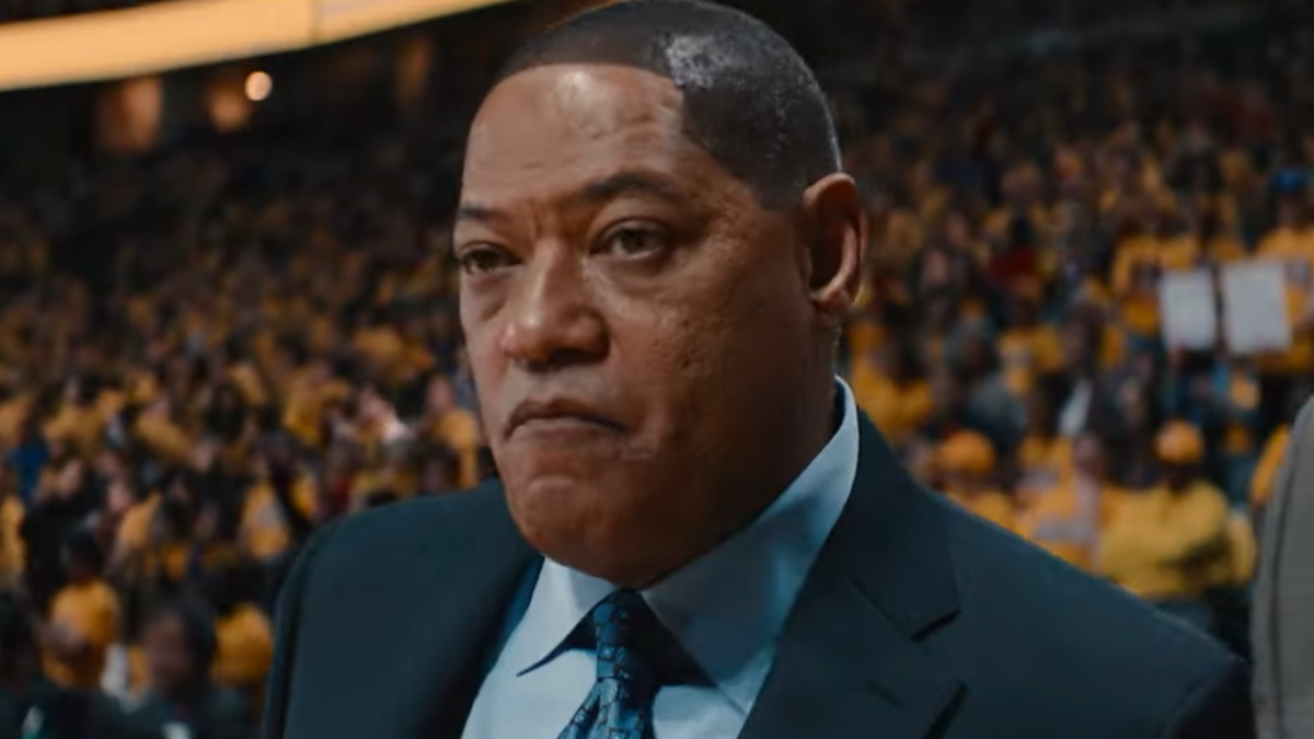 A man dressed in a suit and tie stands in a crowded arena with a serious expression