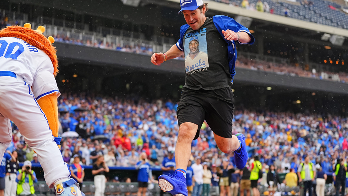 Paul Rudd runs the bases in sports attire during a baseball game as a mascot follows