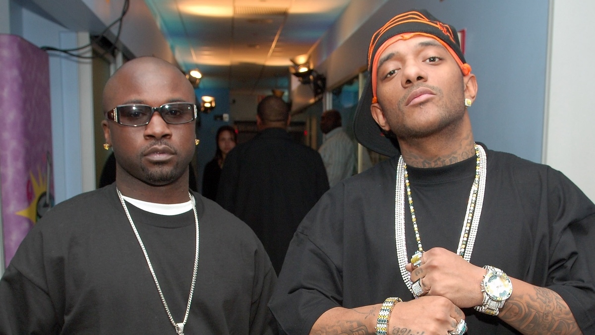 Two men posing, one in a beanie and sunglasses, the other in a bandana, both wearing necklaces