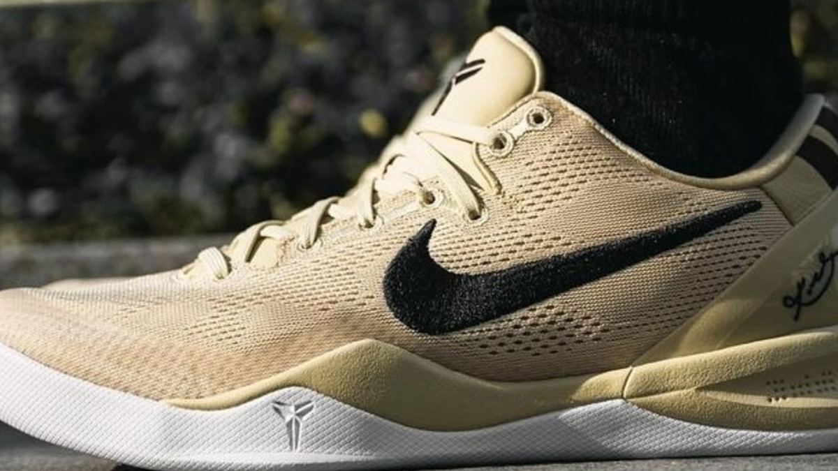 Close-up of a person wearing beige Nike sneakers with a signature black swoosh and a Kobe Bryant logo on the toe and sole