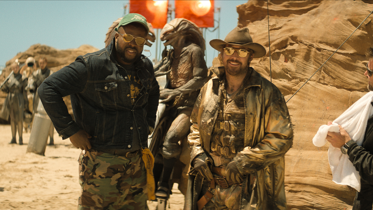 Two actors dressed as a cowboy and military-style on set, surrounded by crew and film equipment