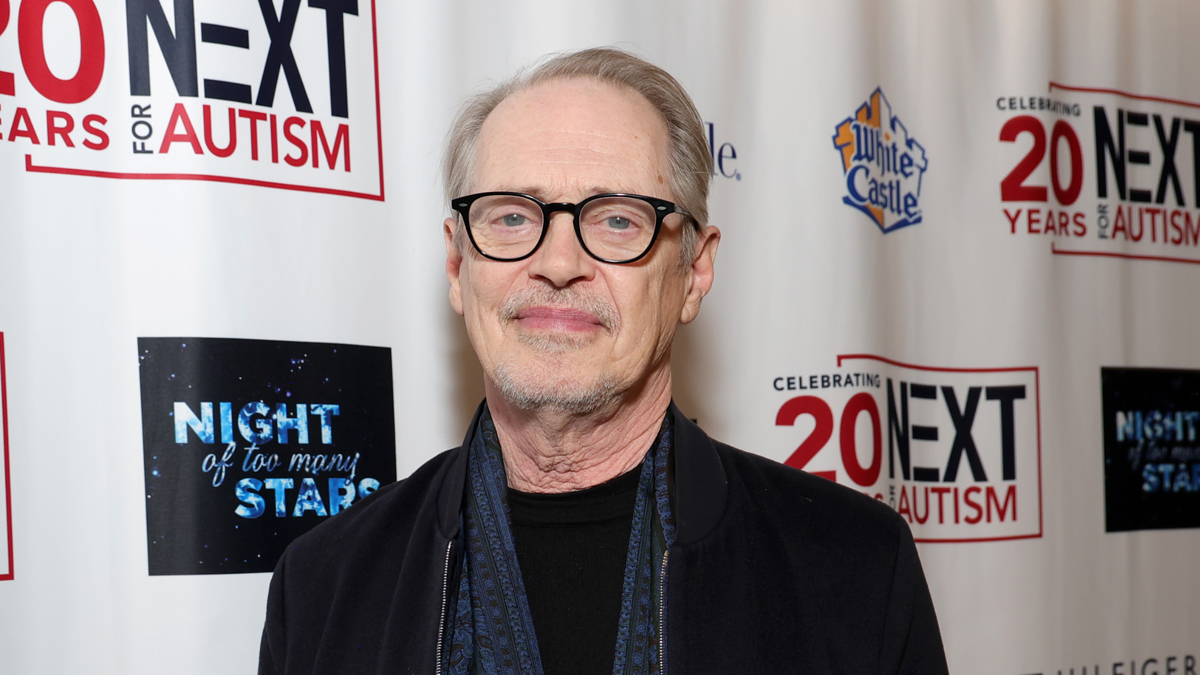 Man in glasses and a scarf smiles at a "Night of Too Many Stars" event