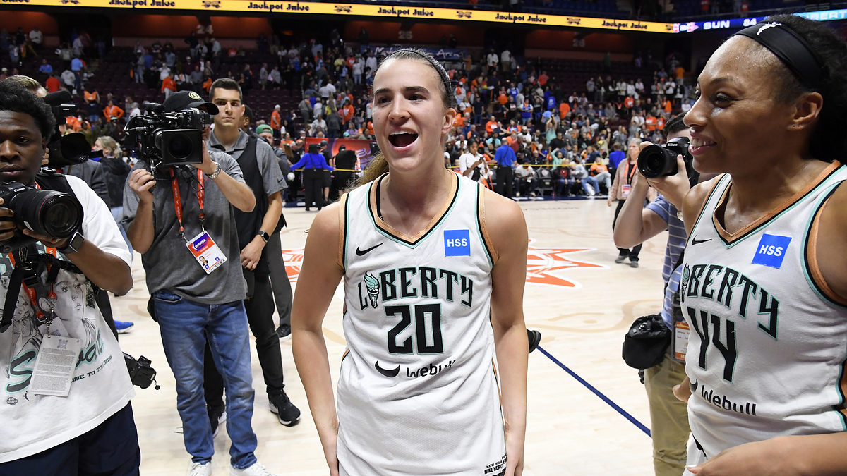 Basketball players on court celebrating victory with press photographers around