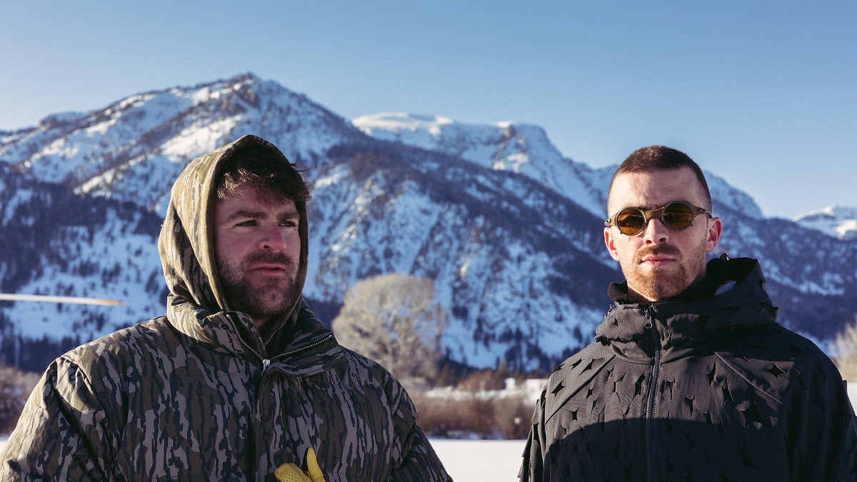 Two men in winter gear standing before snowy mountains