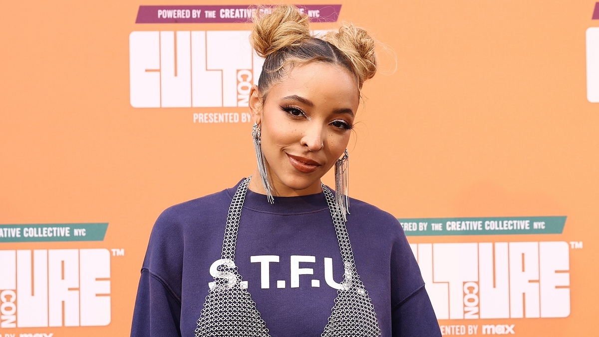 Tinashe on the red carpet at CultureCon, wearing a shirt with "S.T.F.U" text and large dangling earrings
