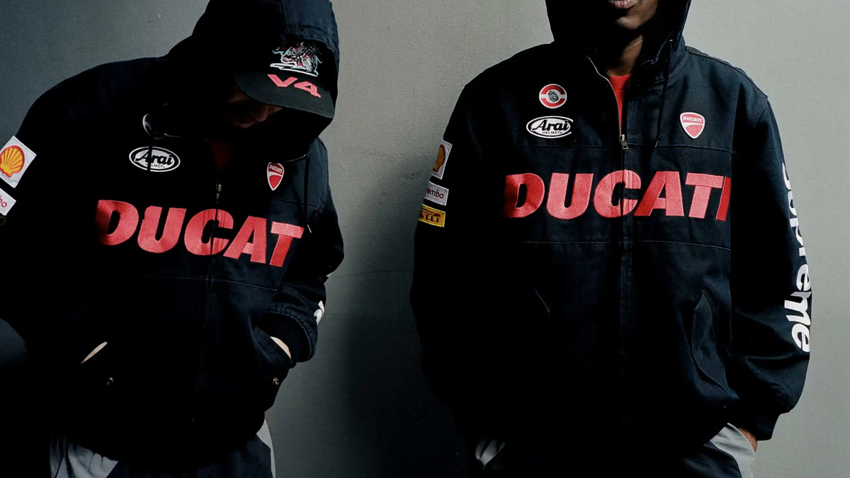 Two people in hooded Ducati racing jackets with patches pose against a plain backdrop