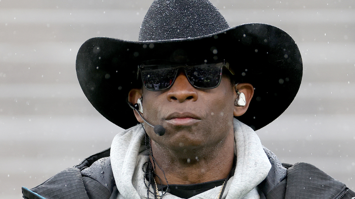 Person in cowboy hat and sunglasses, with earphones, and a rucksack. Raindrops are visible around them