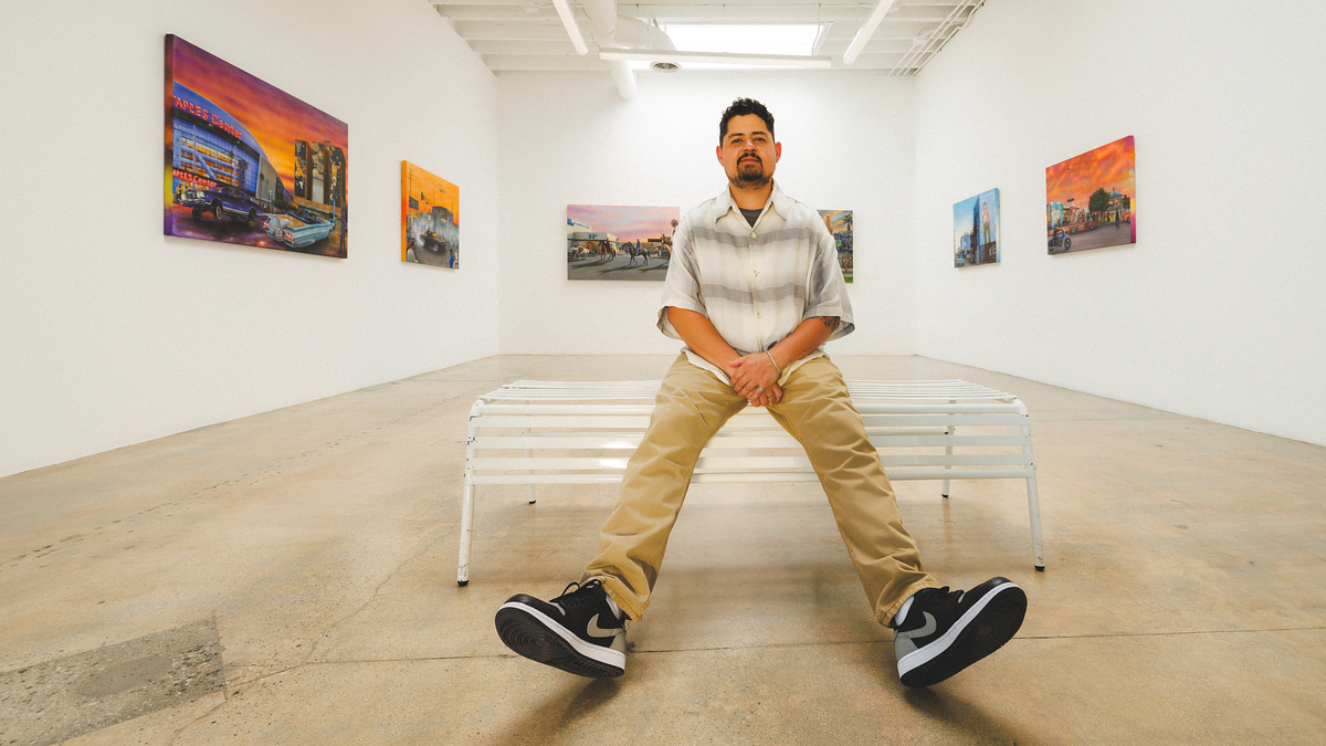 Man seated on a bench in an art gallery showcasing paintings, focusing on his sneakers