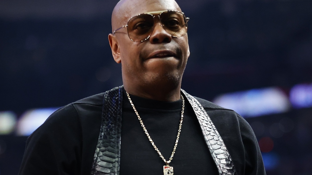 Man in glasses wearing a chain necklace and a black shirt with a textured design at a sporting event