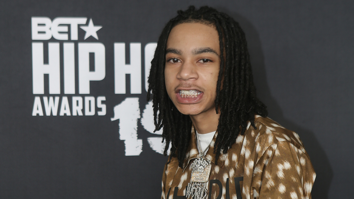 Individual posing at the BET Hip Hop Awards, wearing a patterned jacket and layered necklaces