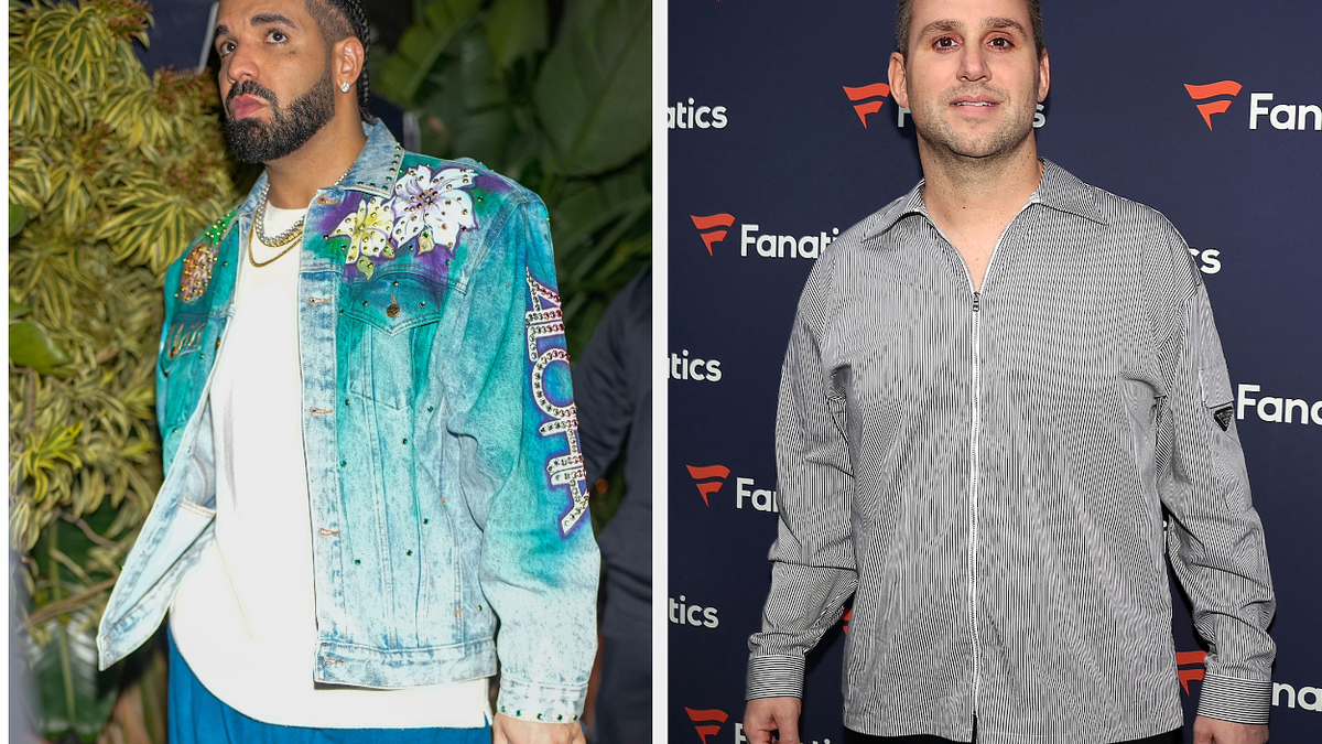 Drake in a detailed denim jacket and white shirt, next to Michael Rubin in a checkered shirt at a Fanatics event. Both are standing and posing for photos
