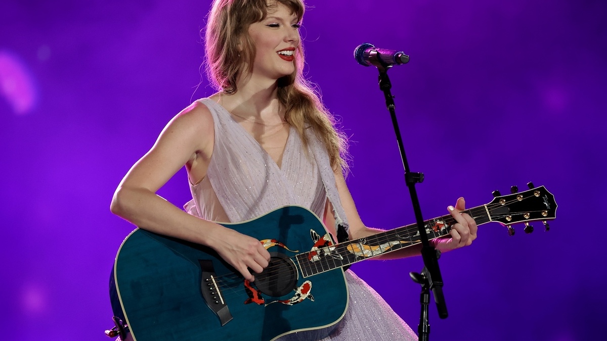 Woman on stage playing guitar and singing into microphone, wearing a shimmery dress
