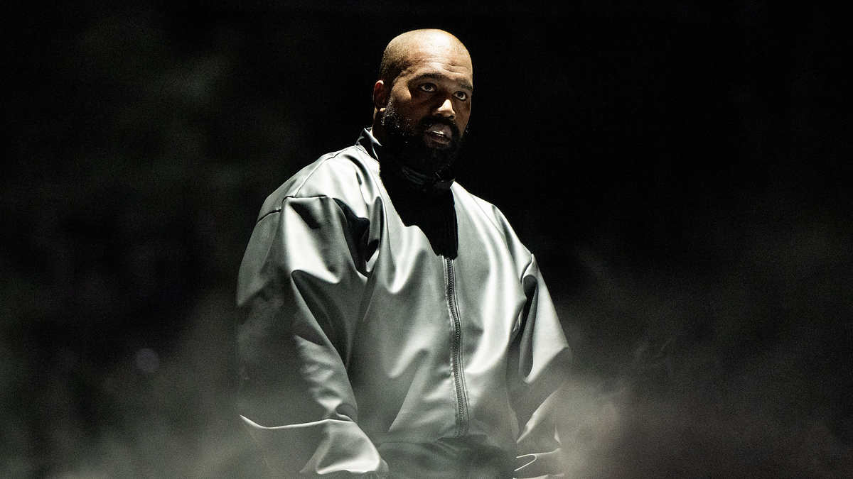 Music artist in a spotlight on stage with a solemn expression, wearing a loose-fitting jacket