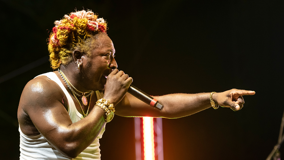 Person with micro braids hair performing on stage with a microphone, wearing a tank top and jewelry