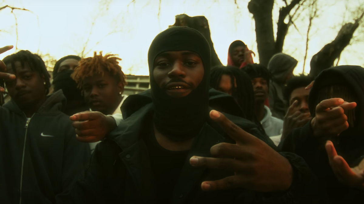 Group of people with focus on individual in center making hand gestures, possibly a music artist with fans or entourage