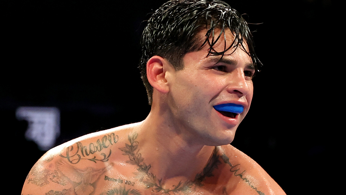Boxer with mouthguard visible, tattoos on chest and arms, wet hair, in the ring