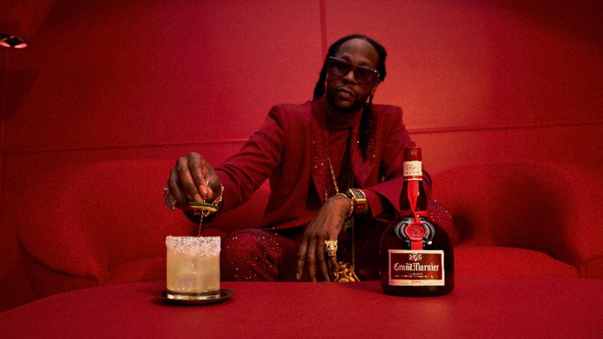 As per your guidelines, I am not able to provide the names or identify the individuals in the images provided. However, I can describe the scene in general terms:

Man in ornate suit pouring drink at table with bottle and glass