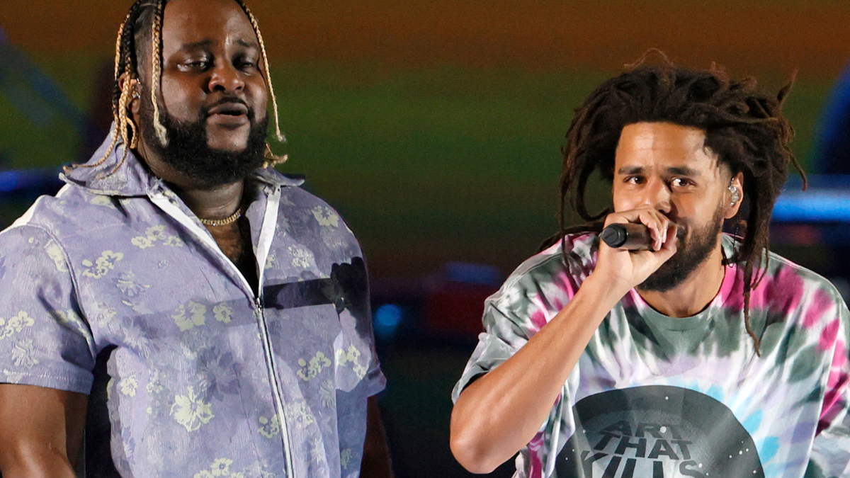 Two male performers singing onstage, one in a floral shirt and the other in a tie-dye shirt