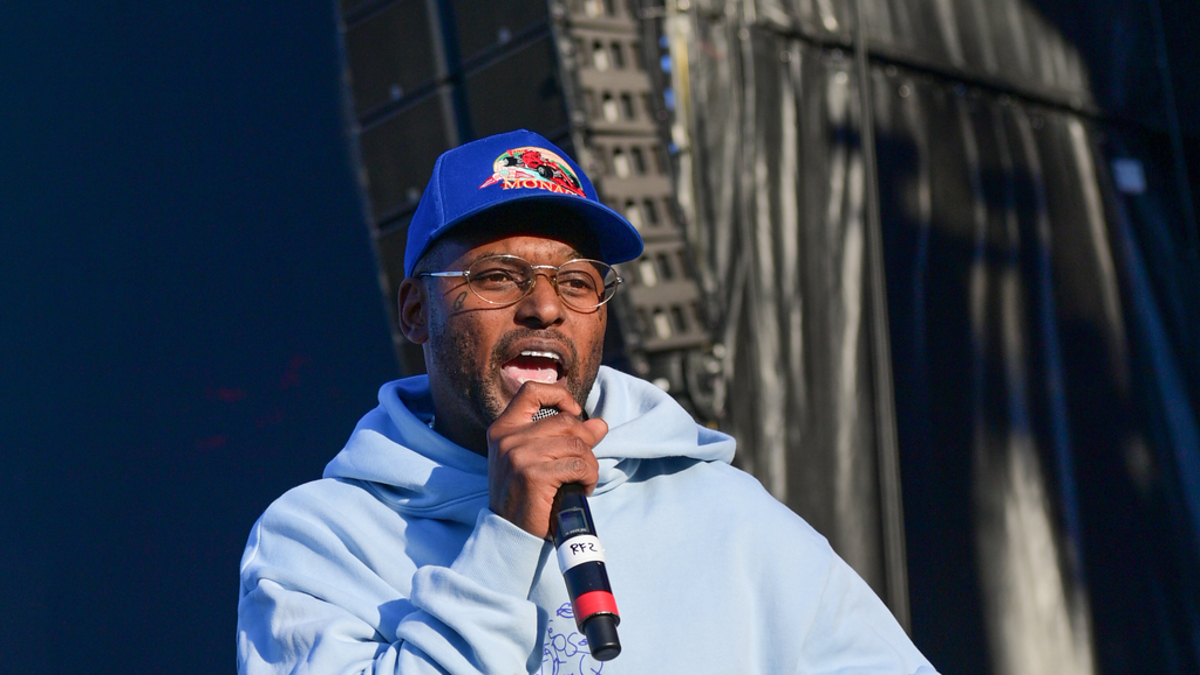 A person in a hoodie and baseball cap speaks into a microphone on stage