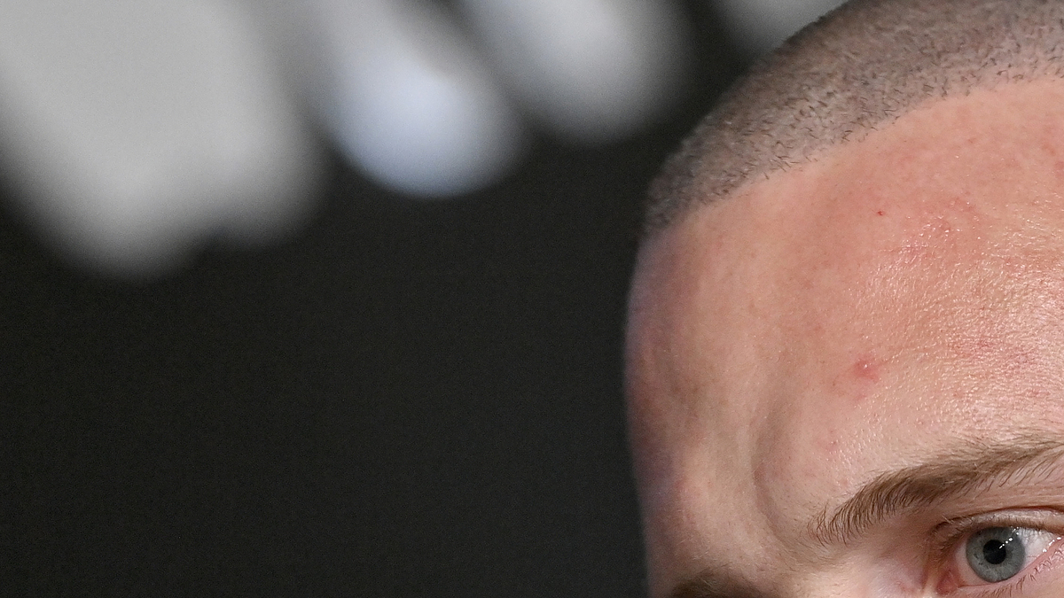 Chet Hanks in a close-up shot, wearing a dark suit at a public event, sporting a shaved head and a neck tattoo